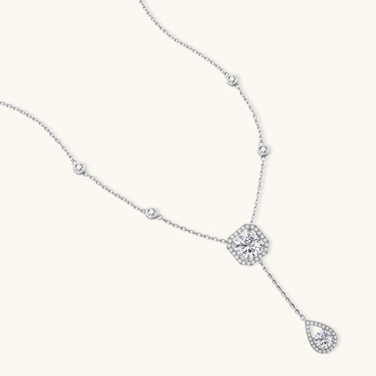 Sterling silver necklace with cushion-cut moissanite halo pendant and teardrop drop on white background