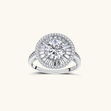 Brilliant round moissanite center stone with baguette and round halo accents in sterling silver setting on light background.