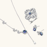 Sterling silver jewelry set with rainbow moissanite stones in clover and butterfly designs on cream background