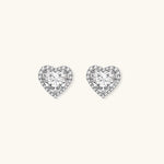 Close-up of heart-shaped moissanite stud earrings in sterling silver halo setting on cream background.