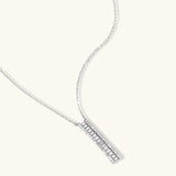 White gold plated necklace with vertical cubic zirconia pendant and matching hoop earrings on neutral background