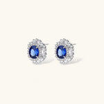 White gold plated jewelry set with blue cubic zirconia centers surrounded by clear crystal halos on cream background.