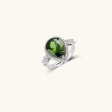 White gold plated jewelry set with green teardrop gemstones and cubic zirconia halos on cream background.