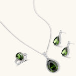 White gold plated jewelry set with green teardrop gemstones and cubic zirconia halos on cream background.