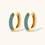 Gold-plated curved necklace and hoop earrings with turquoise cubic zirconia stones on white background.