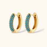 Gold-plated curved necklace and hoop earrings with turquoise cubic zirconia stones on white background.
