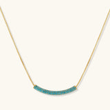 Gold-plated curved necklace and hoop earrings with turquoise cubic zirconia stones on white background.