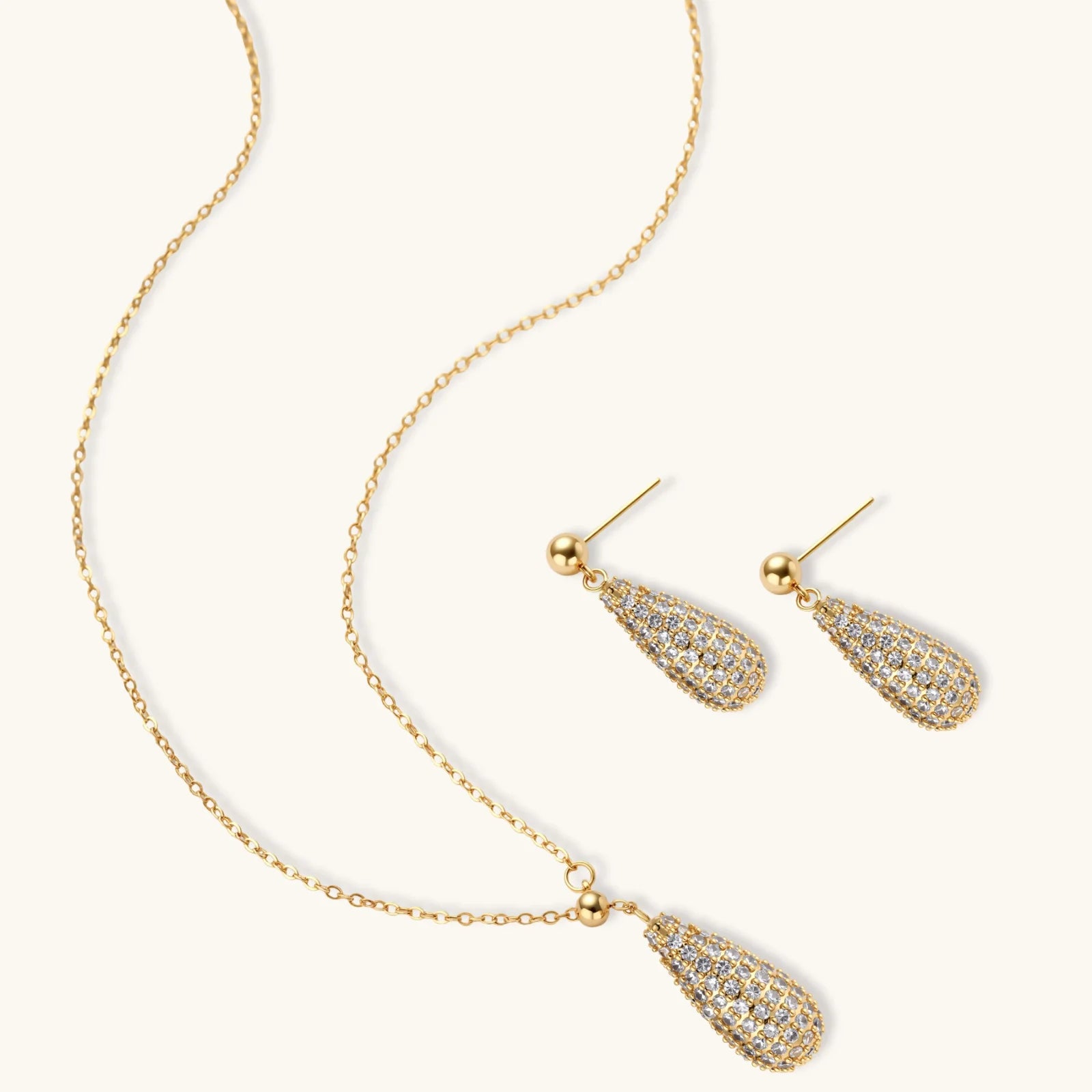 Gold-plated teardrop necklace and earrings covered in AAA cubic zirconia crystals on cream background.