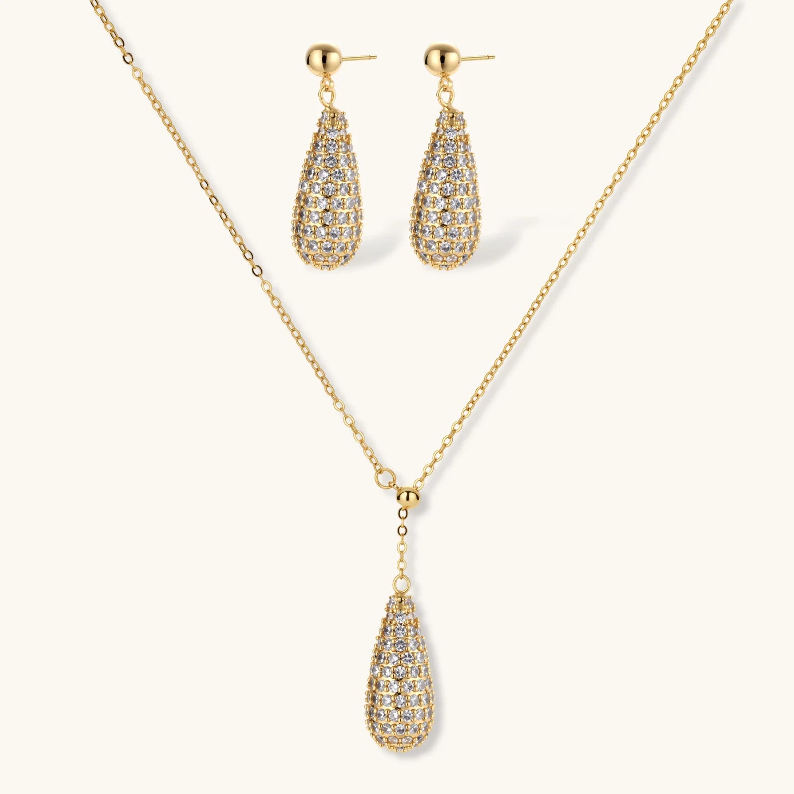 Gold-plated teardrop necklace and earrings covered in AAA cubic zirconia crystals on cream background.