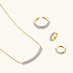 Gold-plated curved necklace, hoop earrings, and adjustable ring with pavé cubic zirconia stones on cream background.