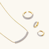 Gold-plated curved necklace, hoop earrings, and adjustable ring with pavé cubic zirconia stones on cream background.