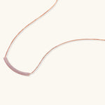 Rose gold jewelry set with pavé cubic zirconia stones including curved necklace, hoop earrings, and adjustable ring on cream background.