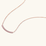 Rose gold jewelry set with pavé cubic zirconia stones including curved necklace, hoop earrings, and adjustable ring on cream background.