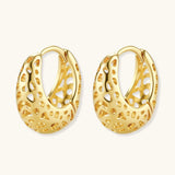 Close-up of small gold-plated hoop earrings with intricate honeycomb cutout pattern on cream background.