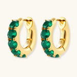 Close-up of gold-plated huggie hoop earrings featuring four emerald green cubic zirconia stones on white background.