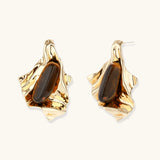 Sculptural stud earrings with organic twisted metal design holding brown gemstones, shown in gold and silver finishes.