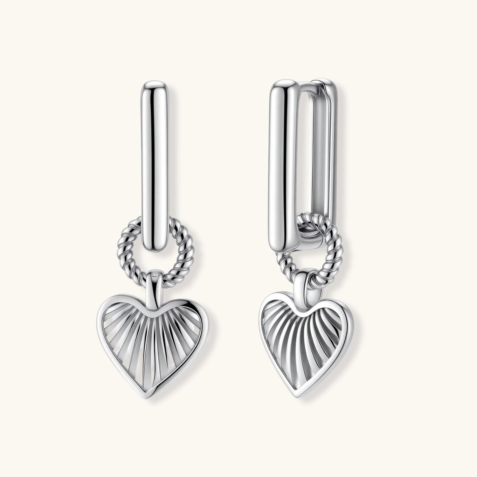 Silver huggie earrings with textured heart charms featuring radial sunburst pattern on neutral background.