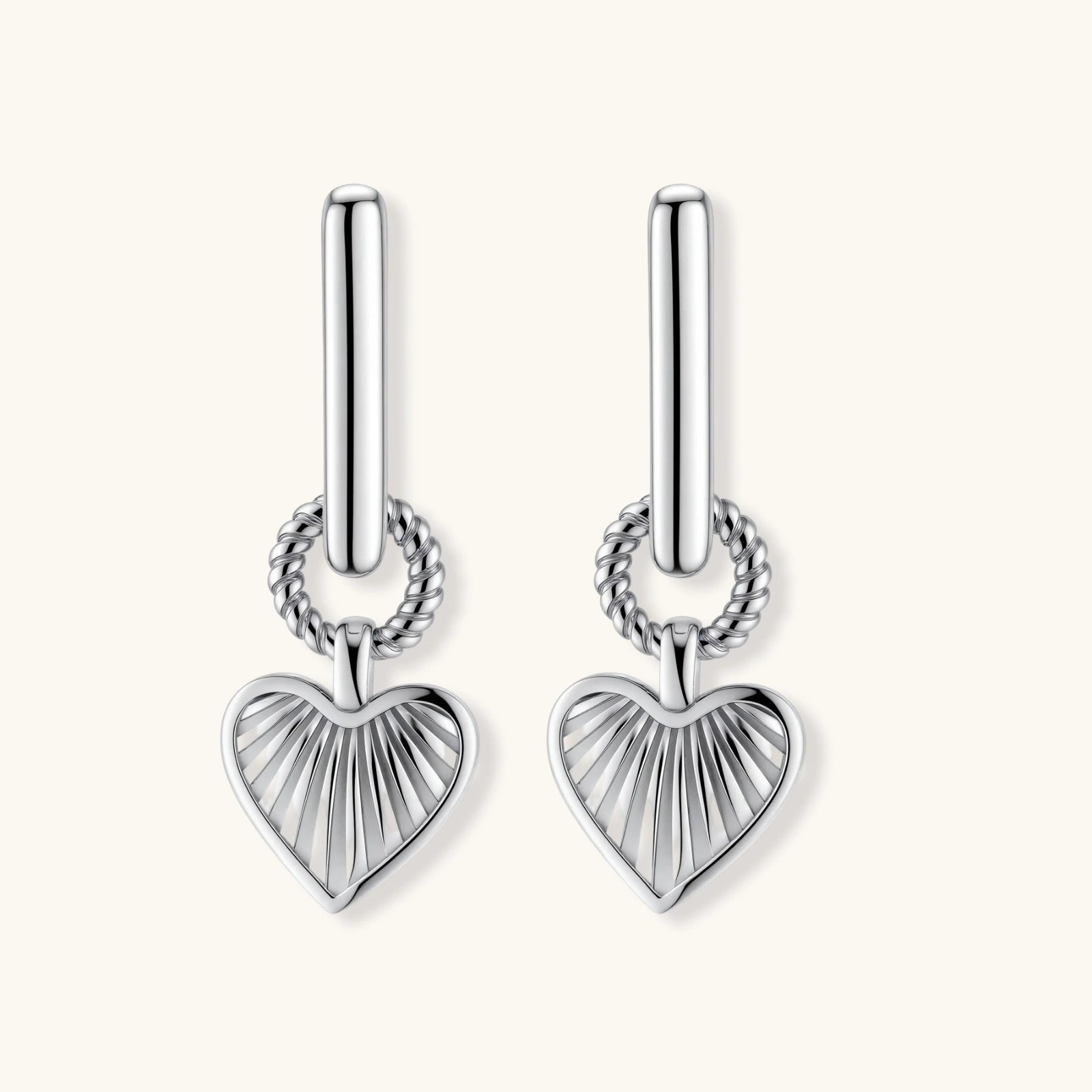 Silver huggie earrings with textured heart charms featuring radial sunburst pattern on neutral background.