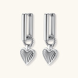 Silver huggie earrings with textured heart charms featuring radial sunburst pattern on neutral background.
