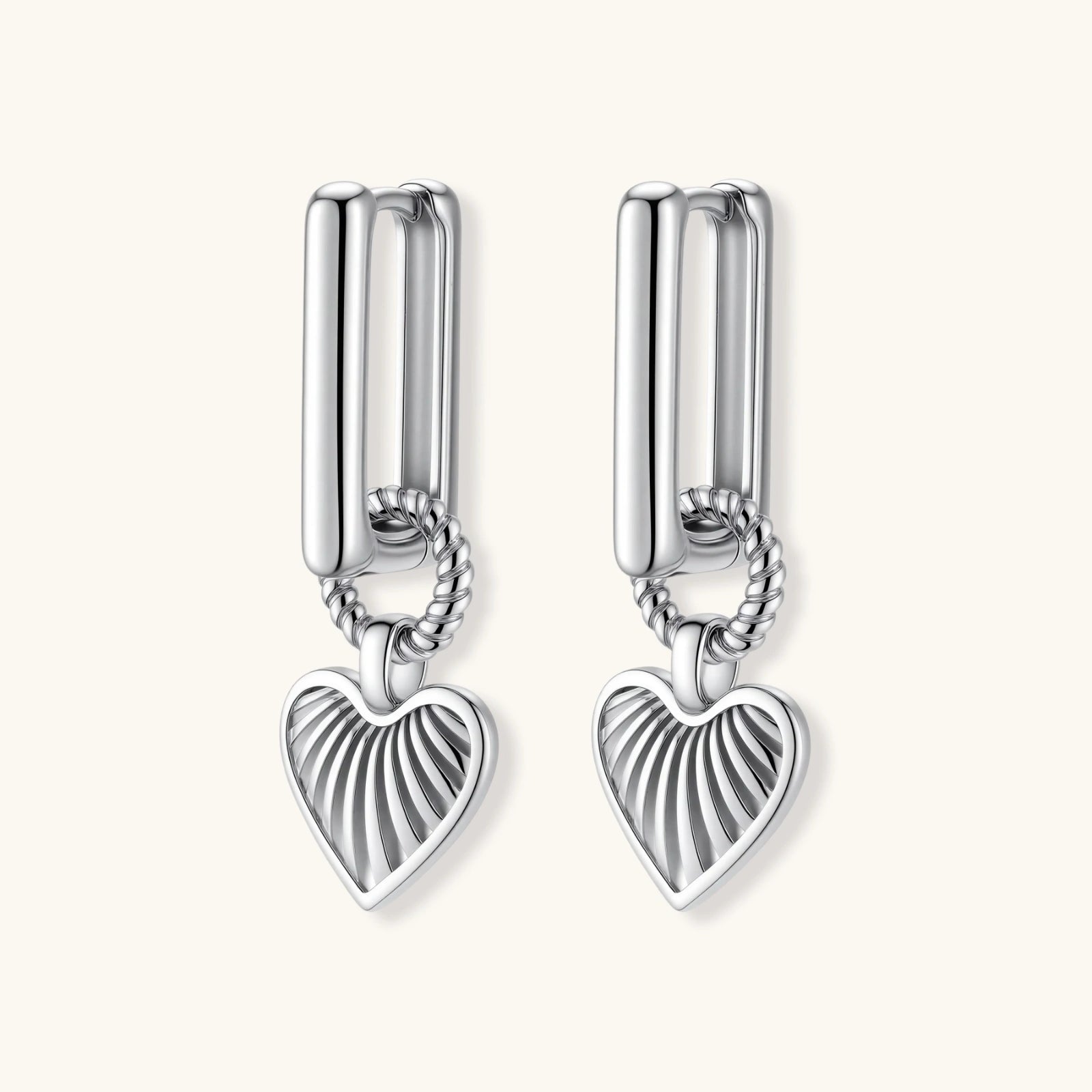 Silver huggie earrings with textured heart charms featuring radial sunburst pattern on neutral background.
