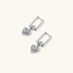 Silver huggie earrings with textured heart charms featuring radial sunburst pattern on neutral background.