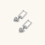 Silver huggie earrings with textured heart charms featuring radial sunburst pattern on neutral background.