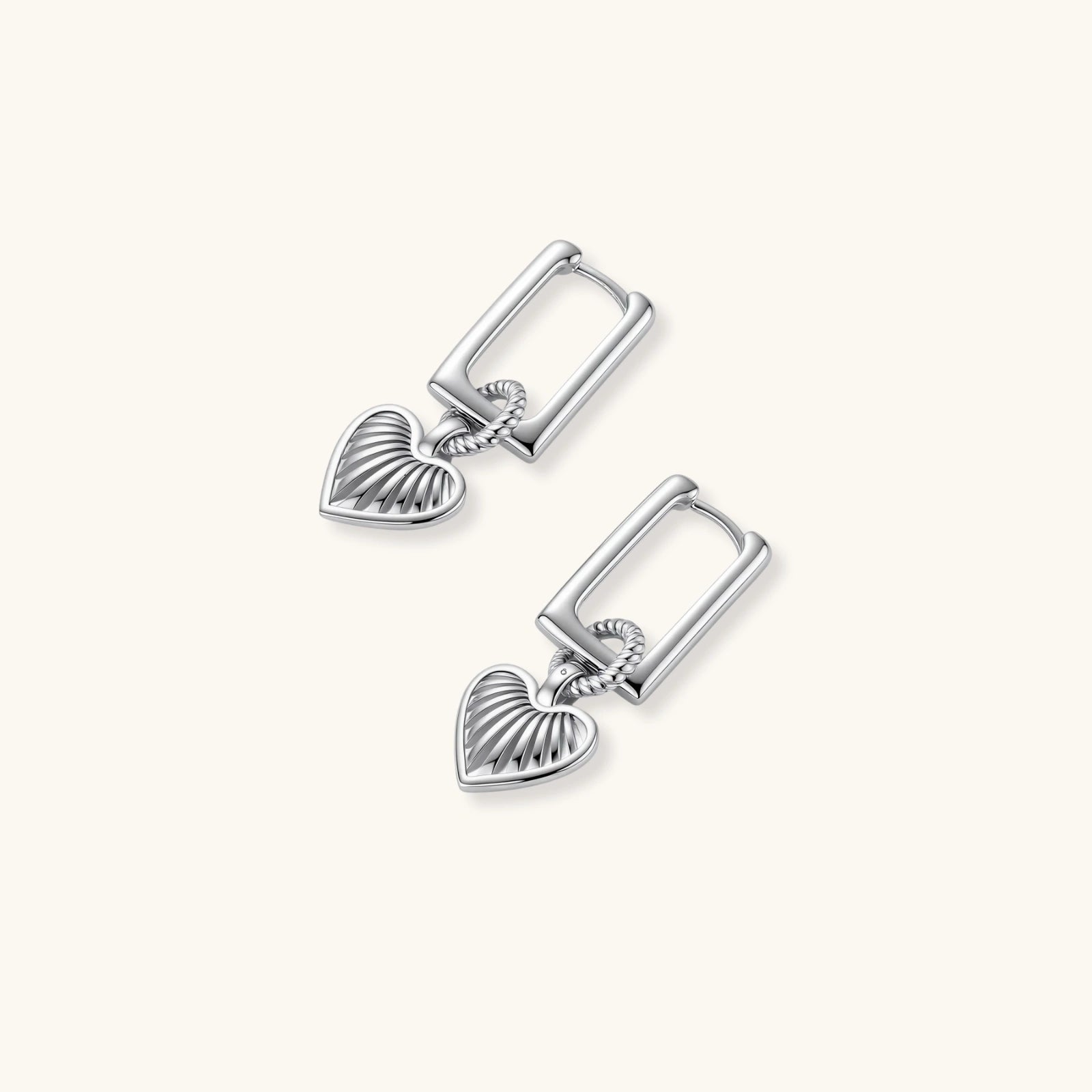 Silver huggie earrings with textured heart charms featuring radial sunburst pattern on neutral background.