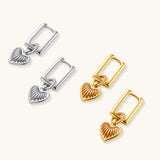 Silver huggie earrings with textured heart charms featuring radial sunburst pattern on neutral background.