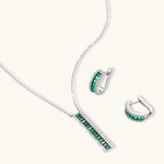 White gold plated jewelry set with emerald green rectangular stones and clear crystals in geometric rows on white background.