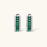 White gold plated jewelry set with emerald green rectangular stones and clear crystals in geometric rows on white background.