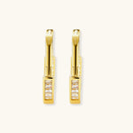 Close-up of gold-plated sterling silver huggie hoop earrings featuring rectangular cubic zirconia stones on neutral background.
