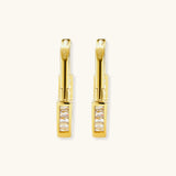 Close-up of gold-plated sterling silver huggie hoop earrings featuring rectangular cubic zirconia stones on neutral background.