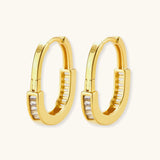 Close-up of gold-plated sterling silver huggie hoop earrings featuring rectangular cubic zirconia stones on neutral background.