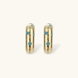Gold-plated huggie hoop earrings with blue star inlays and textured surface, shown against white background.