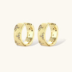 Gold-plated hoop earrings with textured surface and raised floral motifs set with clear zirconia stones on cream background.