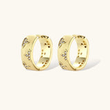 Gold-plated hoop earrings with textured surface and raised floral motifs set with clear zirconia stones on cream background.