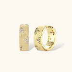 Gold-plated hoop earrings with textured surface and raised floral motifs set with clear zirconia stones on cream background.