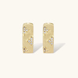 Gold-plated hoop earrings with textured surface and raised floral motifs set with clear zirconia stones on cream background.