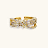 Close-up of gold-plated adjustable ring with crossing bands and sparkling zirconia stones on white background.