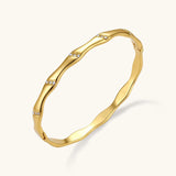 Gold-toned wavy bangle with bamboo-style segments and CZ crystal clusters on cream background. 18K plated stainless steel.