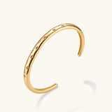 Polished 18K gold plated cuff bracelet with cubic zirconia set in star motifs on a cream background.