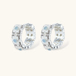 Silver-plated hoop earrings featuring delicate daisy flowers with powder blue centers and crystal accents on white background.