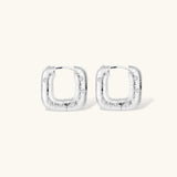 Close-up of ridged silver-plated hoop earrings with embedded crystal details on white background.