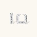 Close-up of ridged silver-plated hoop earrings with embedded crystal details on white background.