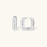 Close-up of ridged silver-plated hoop earrings with embedded crystal details on white background.