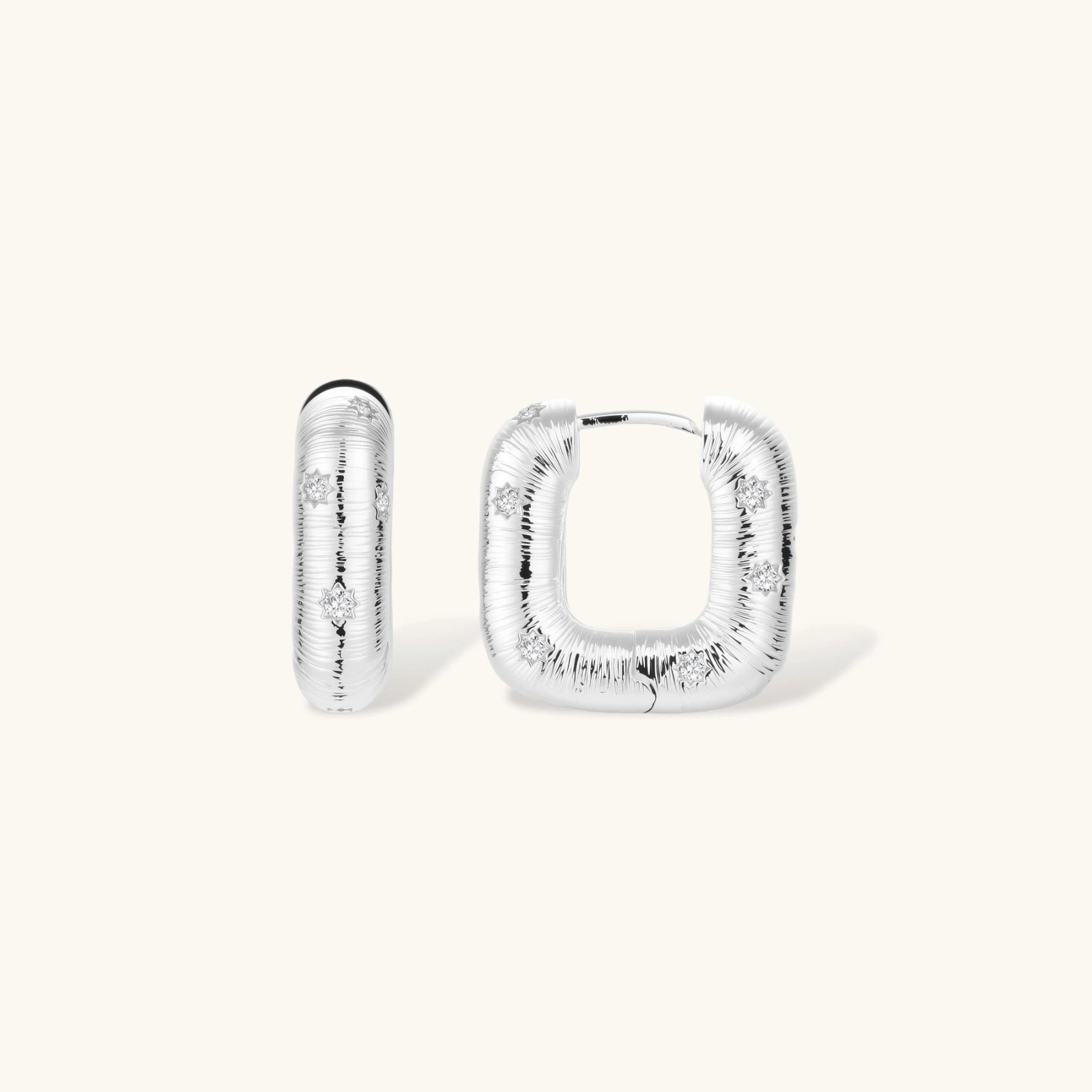 Close-up of ridged silver-plated hoop earrings with embedded crystal details on white background.