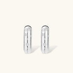Close-up of ridged silver-plated hoop earrings with embedded crystal details on white background.