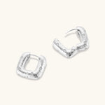 Close-up of ridged silver-plated hoop earrings with embedded crystal details on white background.