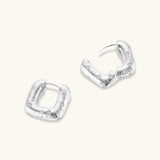Close-up of ridged silver-plated hoop earrings with embedded crystal details on white background.