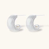 Close-up of small silver-plated hoop earrings with brushed texture and a row of sparkling zircon crystals on white background